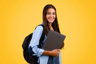 Kendine güvenen Avrupalı genç öğrenci, bilgisayarlı sırt çantalı öğrenci, sarı arka planda izole edilmiş. Yaşam tarzı ve aygıtı, uzaktan öğrenme ve ev ödevi, okulda eğitim, üniversite