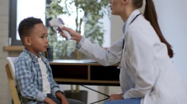 Profesyonel çocuk bakımı. Genç, pozitif kadın pediatrist. Küçük, tatlı Afrikalı Amerikalı çocuğun ciğerlerini kontrol ediyor ve gıdıklıyor. Çocuk babasının bacaklarının üzerinde oturuyor.