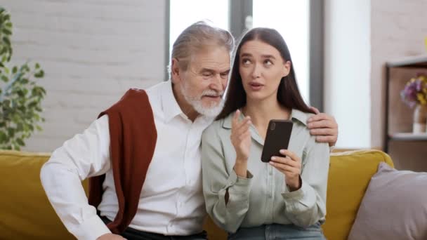 家族のコミュニケーションと近代的な技術 ケアフリーの若い女性は祖父と時間を過ごし スマートフォンでニュースを読み それらを議論します — ストック動画
