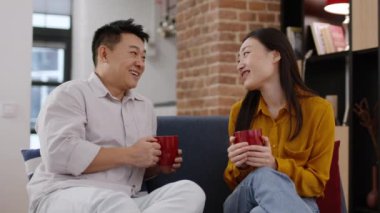 Sağlıklı aile iletişimi. Asyalı erkek ve kadının evde kahve fincanlarıyla konuşması, günlük haberleri tartışması, gülmesi, sohbetin tadını çıkarması, çekim takibi, yavaş çekim.