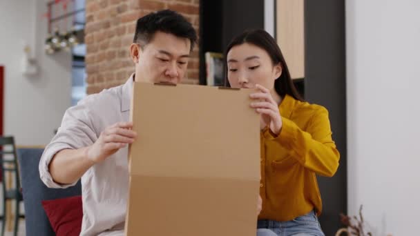 交货很糟糕失望的亚洲已婚配偶打开纸板箱 收到受损物品或不想要的东西 坐在家里沙发上 跟踪镜头 慢动作 — 图库视频影像