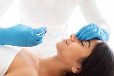 Doktor spa salonundaki genç Hintli kadının burun bölgesine güzellik iğnesi yapıyor. Profesyonel güzellik uzmanının alternatif burun estetiği yaptırdığı güzel bir kadının yakın plan fotoğrafı.