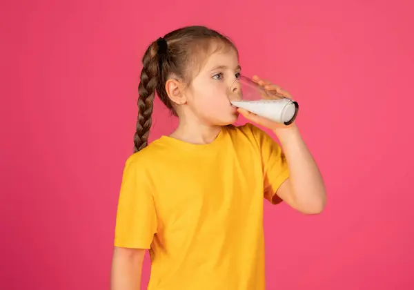 可爱小女孩在玻璃杯中喝牛奶的肖像 站在粉色工作室的背景下 从维生素和矿物质中汲取营养 复制空间 — 图库照片