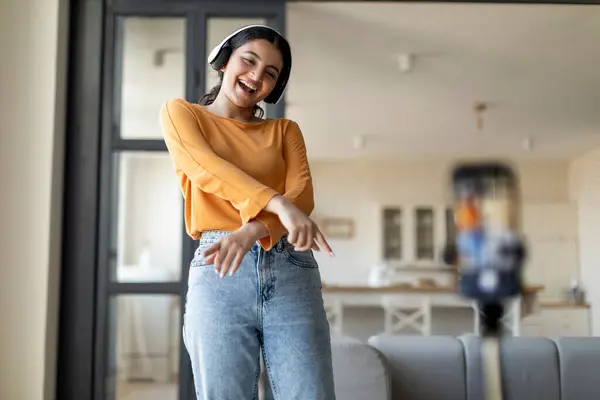 Blogging Concept. Carefree Indian Woman Dancing At Camera, Young Eastern Female Making Funny Dance While Recording Video At Home, Positive Lady Using Smartphone On Tripod, Free Space