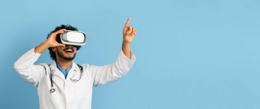 Tıbbi bir buluş. Akıllı, sevimli, Hintli doktor. VR gözlük kullanıyor. Sanal gerçeklikte test yapıyor. Mavi arka planda izole edilmiş.