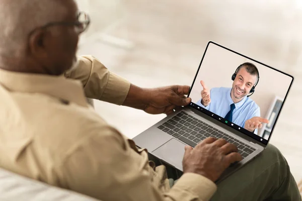 Back View Of Senior Black Man Using Laptop, Have Video Call With Mature Guy Advisor Or Consultant, Sitting Working Online Indoors. High Angle View. Selective Focus On Display