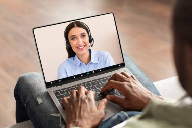 Zenci adam evde telekomünikasyon ekranı olan modern bir bilgisayar kullanıyor kadın iş danışmanıyla görüntülü konuşma yapıyor. Kanepede oturan ve video ekranı olan bir not defteri kullanan tanınmamış bir adam.