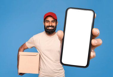 Üniformalı bir Orta Doğulu kurye şablon için büyük boş bir cep telefonu ekranı sunuyor. Çevrimiçi satın alma ve teslimat uygulaması öneriyor. Mavi arka planda bir paket kutusu var. Model