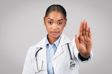 Kendine güveni tam, beyaz önlüklü Afro-Amerikan bayan doktor, gri arka planda, stüdyoda 