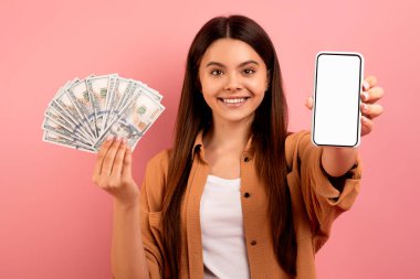 Mobil Bankacılık. Heyecanlı Genç Kız Boş Akıllı Telefon Gösteriyor ve Para Tutuyor, Gülümseyen Kadın Yeni E-Cüzdan Başvurusu Öneriyor, Pembe Stüdyo Arkaplanında Duruyor,