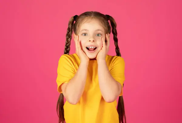 うわー わかった ピンクの背景に隔離された黄色のTシャツを身に着け 幸せなニュースへの反応を表現する 驚きで口を開く彼女の頬の手を持つ楽しい若い少女 — ストック写真