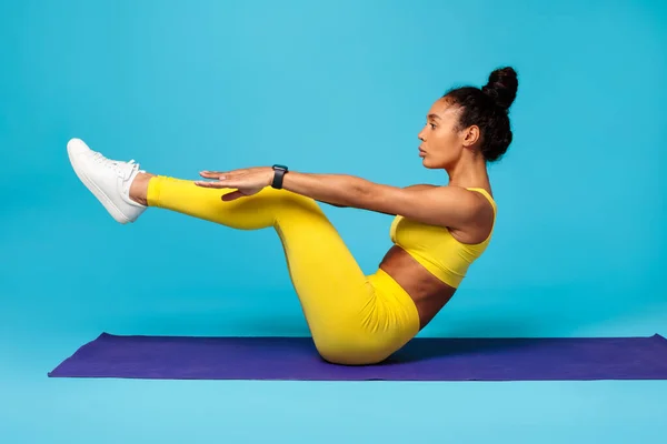 Abs Workout. Fit Black Woman Exercising Sitting In Half Boat Pose Raising Legs, Flexing Abdominal And Core Muscles In Studio On Blue Backdrop. Fitness And Yoga Training. Side View