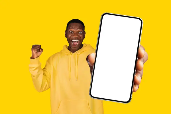 モックアップのための空のスクリーンを備えた大きな携帯電話を保持し モックアップと勝利を象徴し テクノロジーと成功のコンセプトに最適な黒人男性 黄色のスタジオの背景 — ストック写真