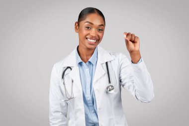Genç siyahi bayan doktorun ilaç kapsülü göstermesine, tedavi önermesine, gri arka planda, stüdyoda izole edilmesine sevindim. Tıbbi yardım, sağlık, ilaç, ağrı kesici, vitamin ve antidepresan.