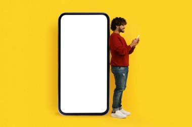 Gündelik kıyafet giyen genç Hintli adam reklam için beyaz ekran fotokopi alanı modeliyle büyük bir telefonun yanında duruyor. Cihaz akıllı telefon kullanıyor, internette çalışıyor, arkadaşlarıyla sohbet ediyor.