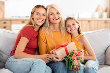 Mutlu aile, hediyeler ve gülümsemeler, ev içi. Güneşli bir öğleden sonra, Uluslararası Kadınlar Günü 'nü kutlayan, büyük anne ve çocuk arasında dokunaklı bir kucaklaşma.