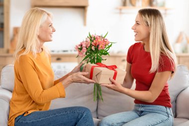 Sevgi dolu genç yetişkin kadın çocuğu, heyecanlı yaşlı anneyi evde doğum günüyle kutluyor. Gülümseyen yetişkin kız milenyum kızı yaşlı annelere hediye olarak kadın gününde çiçek verir.