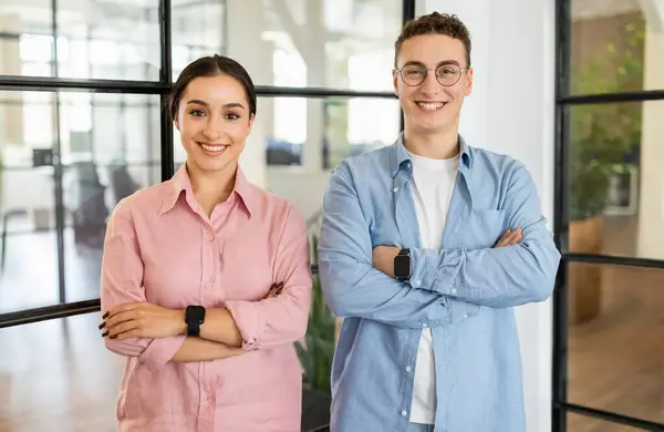 Happy confident young arab woman and european guy manager in casual with crossed arms on chest in coworking office. Startup project, team for work, business together, lifestyle
