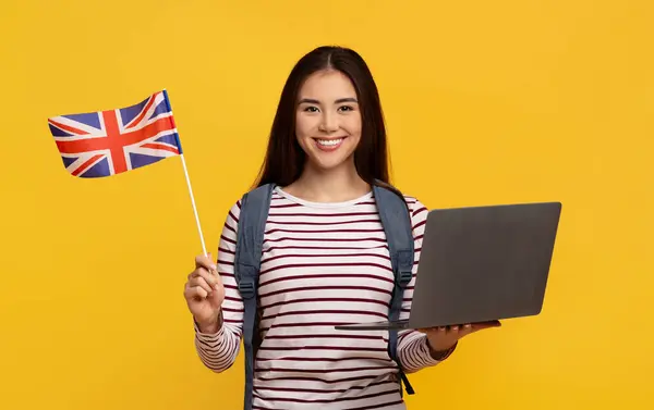 可爱的年轻的亚洲女学生 带着笔记本电脑和英国国旗 在黄色的工作室背景下摆出孤立的姿势 在网上学习英语 国外教育 学生移民 — 图库照片