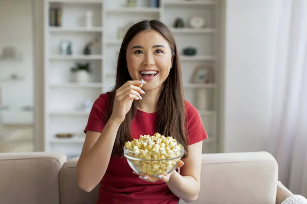 映画の時間だ 幸せなアジアの女性はポップコーンを食べて家でテレビを見ている 快適なリビングルームのインテリアでソファーでリラックスしながらスナックでボウルを抱えている興奮する韓国の若い女性 — ストック写真