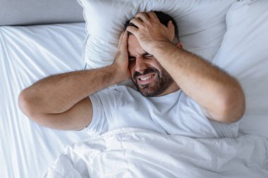 Uykusuz sakallı adam yatakta tek başına uzanıyor yatak odasında başı ağrıyor, migren ve uykusuzluk çekiyor, ağır şeyler düşünüyor. Uyku problemi. Görüntü görüntüsünün üstünde