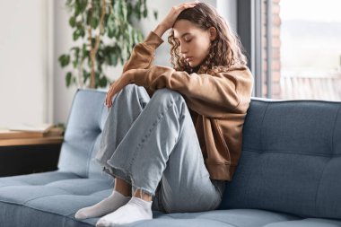 Gençlikte Depresyon. Depresyondaki genç kız üzgün, evdeki koltukta oturan depresif düşünceler yüzünden acı çekiyor. Gençlik Yalnızlığı ve Mutsuzluğu, Akıl Sağlığı Sorunları Konsepti