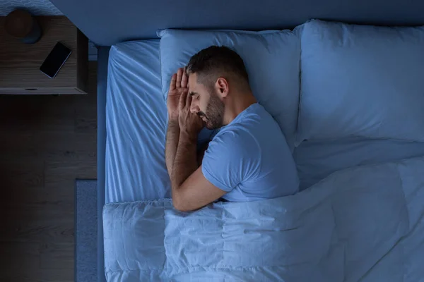 Guy Sleeping Holding Hands Near Face Enjoying Rest Lying In Cozy Bed In Modern Bedroom Interior. European Middle Aged Guy Napping At Night. Recreation And Healthy Sleep Concept. Low Light, Top View