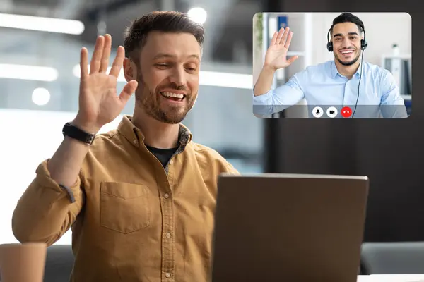 Happy Entrepreneur Man Waving Hello To Laptop Computer Making Video Call Sitting In Modern Office. Businessman Communicating Online At Workplace. Distance Communication Concept