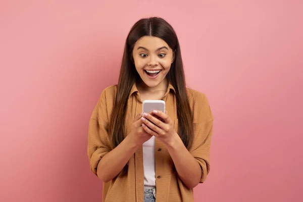 移动报价 惊讶地看着智能手机屏幕的少女兴奋地 快乐的少女对好消息的情绪反应 站在那里张开嘴 粉红相间 复制空间 — 图库照片