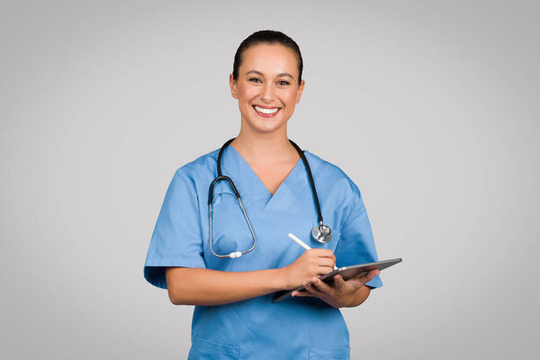 Friendly female nurse in blue scrubs holding digital tablet, embodying modern healthcare technology with bright, approachable demeanor