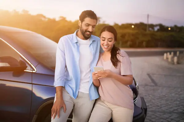 Casal Árabe Sorridente Apoiando Seu Carro Entardecer Olhando Para Smartphone — Fotografia de Stock