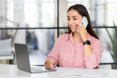 Milenyum Avrupalı iş kadını yöneticisinin akıllı telefondan aramasına, konuşmasına, modern ofisteki bilgisayar laptopuna bakmasına sevindim. Planlama işi, iş iletişimi, çoklu görev, iş hayatı