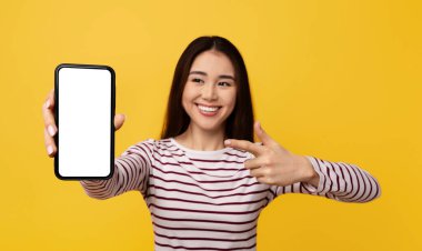 Heyecanlı, güzel, Asyalı kız öğrenci elinde beyaz ekranla kocaman bir telefon gösteriyor. İnternetten güzel bir teklif, anlaşma, sarı stüdyo geçmişi öneriyor. Mobil uygulama