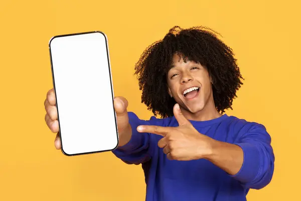 网上广告 快乐的黑人男人站在黄色工作室的背景上 手里拿着空白智能手机指指指点点 快乐的非洲裔美国人推荐新的应用程序或网站 — 图库照片