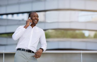 Modern ofis merkezinin yakınlarında cep telefonuyla konuşan gülümseyen siyahi iş adamının portresi, Mutlu Afrikalı Amerikalı Erkek Girişimci Cep Telefonu Konuşması, Kopya Boşluğu