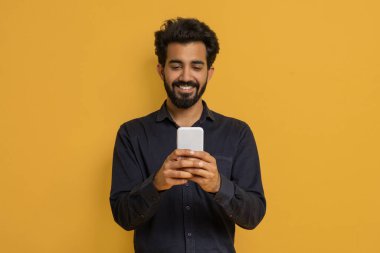 Gülümseyen Hintli genç adam Modern Akıllı Telefon kullanarak Sarı Arkaplan 'a Karşı, Mutlu Doğulu Adam Cep Telefonu Mesajları, Yeni Uygulamayı kontrol ediyor, Sarı Arkaplanda Duruyor, Boşluğu Kopyalıyor