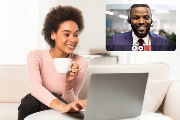 Positive african american lady have video call with colleague man in suit while working remotely, sitting on couch at home, drinking tea, using laptop. Telecommunication concept