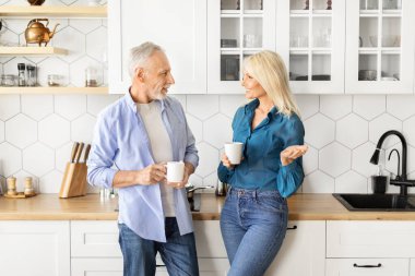Modern mutfağın içinde kahvemizi yudumlarken gülümseyen kıdemli erkek ve kadın, mutlu yaşlı eşler evde gündelik sohbetlerin keyfini çıkarıyorlar, sohbet ediyorlar ve birbirlerine gülümsüyorlar, bedava uzay.