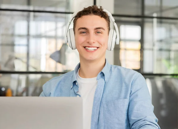 Happy millennial caucasian man manager in headphones work at computer, listen music, has video call in coworking office, close up. Work and service, business remotely with technology