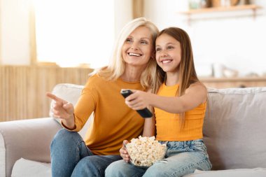 Evde film izleyen mutlu torun ve büyükanne. Neşeli genç kız büyükannesiyle vakit geçiriyor, TV 'de çizgi film seçiyor, patlamış mısır yiyor, fotokopi çekiyor.
