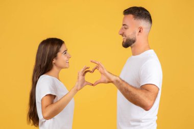 Binlerce yıllık Avrupalı eş ve koca, elleriyle kalp jesti yapıyor, hassas anın tadını çıkarıyor, sevgi dolu, sarı stüdyo arka planında soyutlanmış bir şekilde. Tarih ve romantik yaşam tarzı
