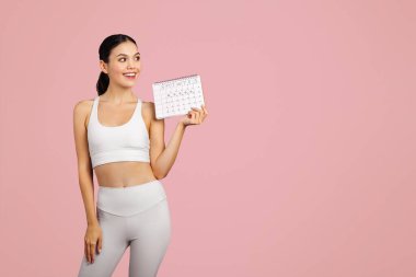 Spor giyim takvimindeki genç Avrupalı zayıf kadın, pembe stüdyo arka planında izole edilmiş, boş alan. Spor ve regl, kilo kaybı ve vücut bakımı yönetimi, sağlık hizmetleri