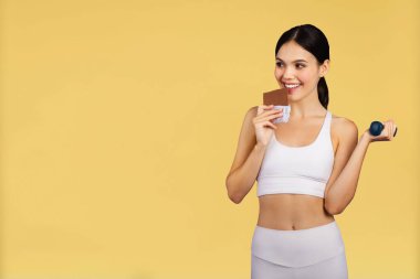 Sarı stüdyo arka planında izole edilmiş dambıl yiyen neşeli beyaz kadın. Diyet, reklam ve teklif, pilates fitness ve vücut bakımı, seçim ve spor