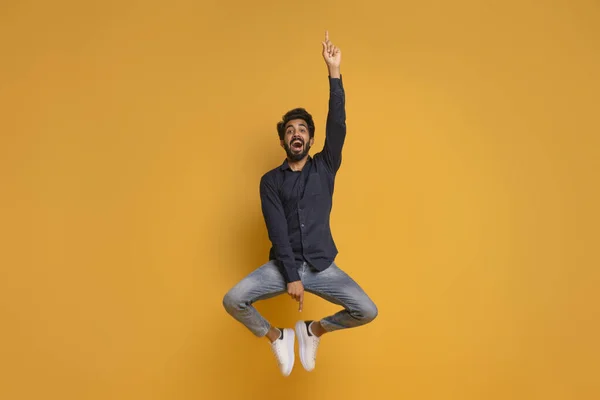 看看这个快乐的印度年轻人在空中跳来跳去 在黄色的工作室背景上展示免费的复制空间 全长镜头 — 图库照片
