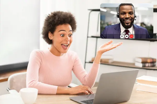 Glad surprised millennial african american business lady has video call gesturing, look at laptop webcam, sitting at table in office interior. Business, work, meeting remotely and social distancing