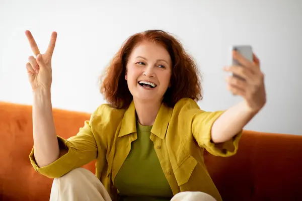 Blogging For Seniors. Positive Elderly Woman Taking Selfie On Smartphone And Showing Peace Gesture, Happy Cheerful Older Lady Having Fun While Capturing Photos, Posing At Camera, Closeup Shot