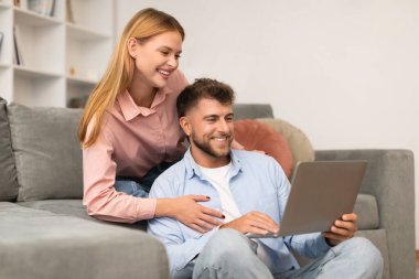 Genç karı koca internet sitelerine girip dizüstü bilgisayarda film izliyorlar, birlikte vakit geçiriyorlar, evdeki kanepede dinleniyorlar. Rahatlama boş zamanı ve dijital bağlantı