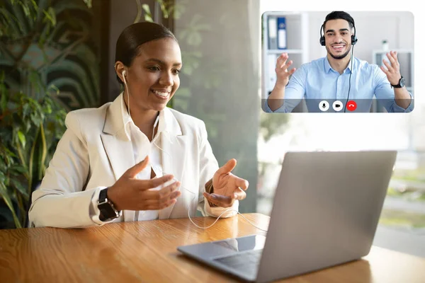 Glad surprised millennial business lady has video call gesturing, look at laptop webcam, sitting at table in office interior, using earphones. Business, work, meeting remotely and social distancing