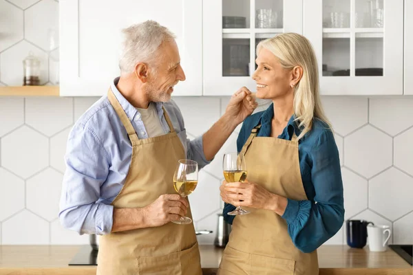 Domestic Romance. Happy Senior Couple With Wine Glasses Relaxing In Kitchen Interior, Romantic Older Man And Woman Having Date At Home, Enjoying Spending Time Together, Closeup Shot