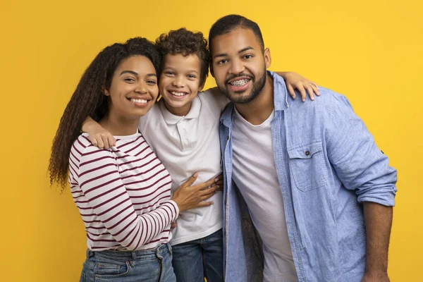 イエロースタジオの背景 フリースペースの上にトゲットするアフリカ系アメリカ人の親を愛し 笑顔の男性の子供を抱きしめ カメラで笑顔の息子と3人の幸せなブラックファミリー — ストック写真